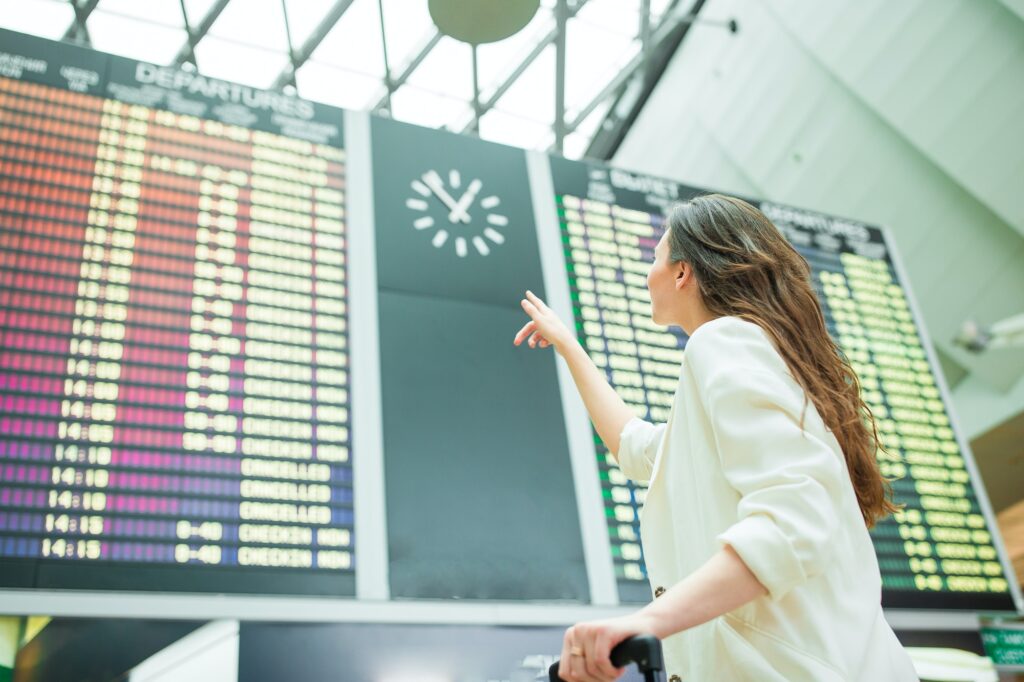 Young woman in international airport looking at the flight information board checking for flight